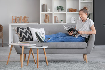 Young woman reading interior design magazine on sofa at home