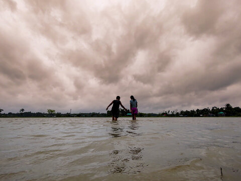 Silhouette of Two People Walking in Flooded Water Under Dramatic Cloudy Sky