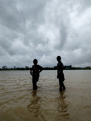 Silhouette of Two People Walking in Flooded Water Under Dramatic Cloudy Sky