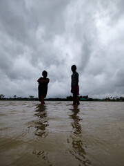 Silhouette of Two People Walking in Flooded Water Under Dramatic Cloudy Sky