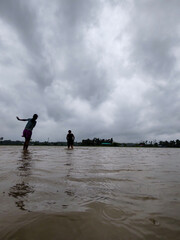 Silhouette of Two People Walking in Flooded Water Under Dramatic Cloudy Sky