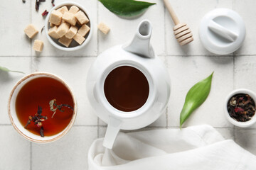 Beautiful composition with teapot, cup of tea and napkin on tile background