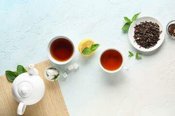 Composition with stylish tea pot, lemon, cups of tea and bamboo mat on light blue grunge background