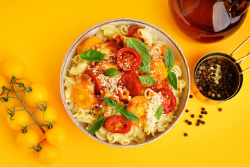 Bowl of tasty pasta with tomato and basil on yellow background