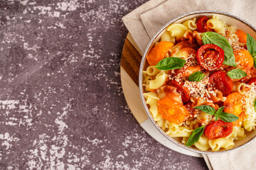 Bowl of tasty pasta with tomato and basil on grunge background