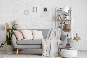 Interior of stylish modern living room with grey sofa and shelving unit near white brick wall