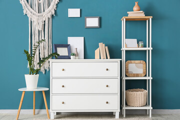 Interior of stylish modern room with commode and shelving unit near blue wall