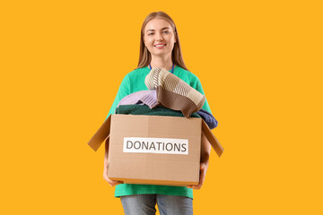 Young female volunteer with donations on yellow background