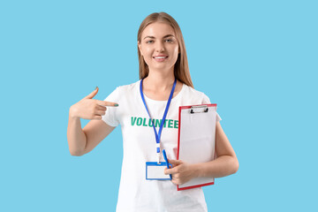 Young female volunteer with donations on blue background