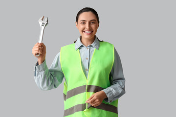 Young female construction worker with wrench on grey background. Woman in male profession concept