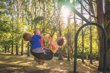Three children swinging on a tyre swing in a playground in summer, USA