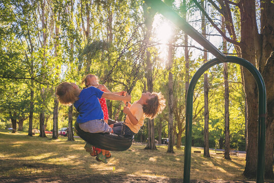 Three children swinging on a tyre swing in a playground in summer, USA - Powered by Adobe