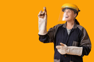 Young female construction worker with protective helmet and gloves pointing at something on yellow...