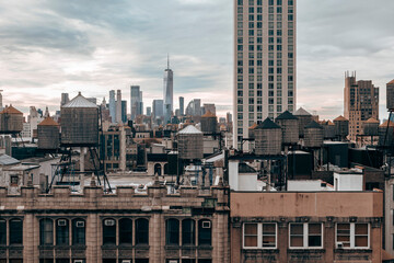 A cloudy New York City skyline featuring iconic rooftop water towers, historic architecture, and modern high-rises, capturing urban contrast