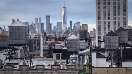A cloudy New York City skyline featuring iconic rooftop water towers, historic architecture, and...