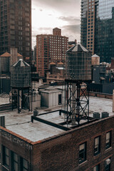 A cloudy New York City skyline featuring iconic rooftop water towers, historic architecture, and modern high-rises, capturing urban contrast