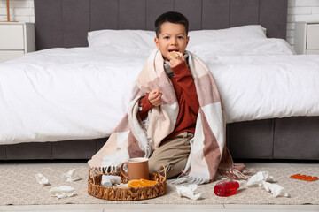 Ill little Asian boy with sore throat eating lemon in bedroom