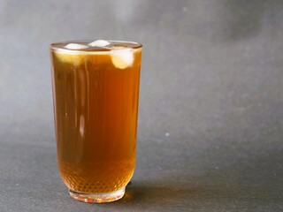 A refreshing glass of iced tea, elegantly served in a crystal clear glass. The amber hue of the iced tea contrasts beautifully with the clarity of the glass. A classic iced tea, isolated gray