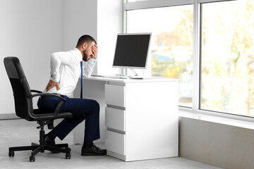 Young businessman suffering from back pain at table in office