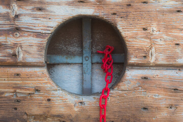 Legame di sangue: una piccola finestra rotonda su un portone di legno con una grata metallica a cui è legata una catena rossa di plastica © Andrea Vismara