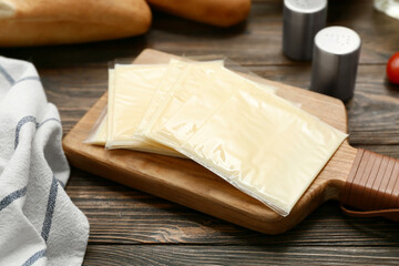 Board with slices of delicious processed cheese on wooden table, closeup