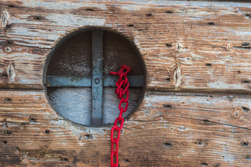 Legame di sangue: una piccola finestra rotonda su un portone di legno con una grata metallica a cui è legata una catena rossa di plastica © Andrea Vismara