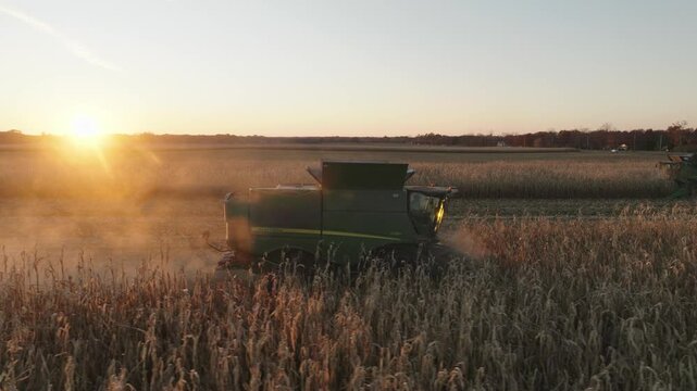 Aerial footage of a combine harvesting corn in a vast rural field during sunset, with warm golden hues and visible farming equipment in action.