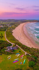 Colorful kayaks arranged on green grass near a coastline at sunset with soft waves and vibrant skies