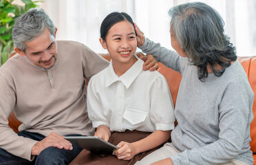 cheerful granddaughter playing on digital tablet with grandparent indoors at home,bonding of two generation meeting on holiday time,family lifestyle,relationship