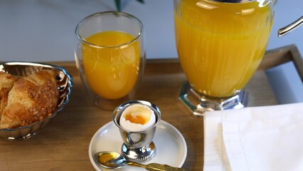  Light breakfast with intricate silver egg holder, golden spoon, glass of orange juice, and crisp croissants, arranged thoughtfully to highlight detailed craftsmanship and elegance.