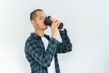 Young asian men wearing flannel and shirt is drinking from black tumbler with smile in isolated white background