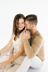 Fototapeta premium Young man and woman are sitting on a white surface, hugging each other. Scene is warm and affectionate