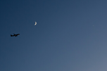 silhouette airplane flies at night towards the moon with a clear sky in dark blue tone and a star....