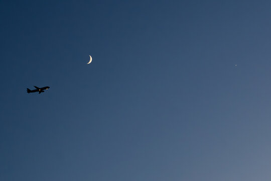 silhouette airplane flies at night towards the moon with a clear sky in dark blue tone and a star. Concept: night flights, vacation, travel.