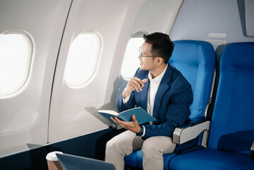 Young Asian executive excels in first class, multitasking with digital tablet, laptop and...