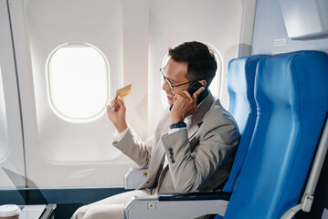 Young Asian executive excels in first class, multitasking with digital tablet, laptop and...