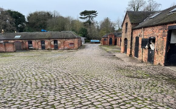 Typical cobbled farm yard with a horse in the stable at Elvaston Castle. Elvaston, Derby, England, UK. December 2024. 