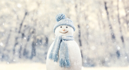 Happy realistic snowman wearing knitted winter scarf and hat with pom pom, outdoors during falling snow. Christmas holiday or winter vacation and cooling and heating temperatures concept