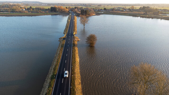 Aerial view of vehicles on A19 main road on raised embankment above flooded landscape 