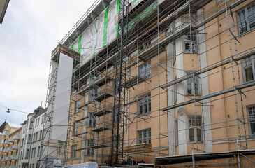 Scaffolding surrounding a beige building under renovation, featuring large windows and an industrial urban setting. Concept of construction