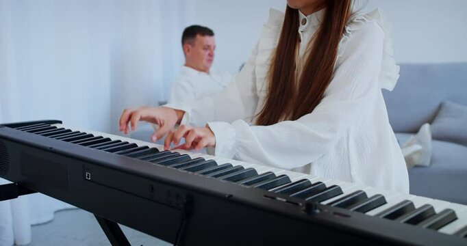 Child musician plays digital piano with father on background. Girl hands press keys, Improving skills of playing musical instrument