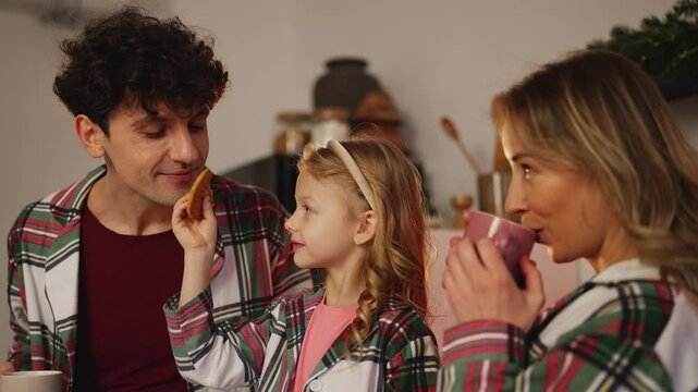 Happy child and her parents eat cookies and drink tea, cherishing time together