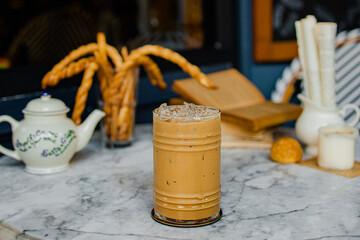 A refreshing iced coffee drink sits on a marble table, accompanied by decorative breadsticks and a teapot, creating a cozy café atmosphere.