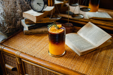 A vibrant cocktail sits on a textured surface, accompanied by a book and clock, creating a cozy, inviting atmosphere.
