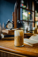 A cozy scene featuring a glass of iced coffee on a rustic table with books and a clock, evoking a warm, inviting atmosphere.