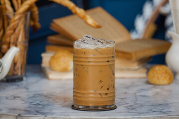 A refreshing iced coffee drink sits on a marble table, surrounded by books and pastries, creating a cozy and inviting atmosphere.