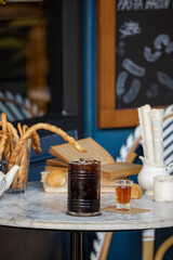 A stylish café table featuring a large glass of dark beverage, a smaller glass, bread, and decorative elements, set against a blue backdrop.