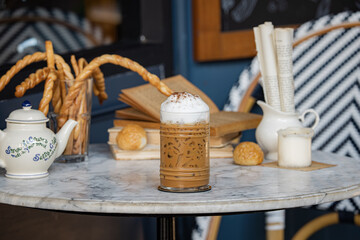 A cozy café scene featuring a frothy beverage, pastries, and decorative items on a marble table, evoking a warm and inviting atmosphere.