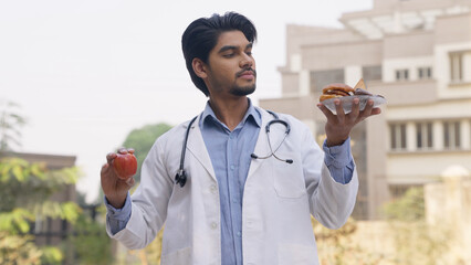 Doctor Holding Apple and Junk Food in Each Hand and Looking at Junk Food