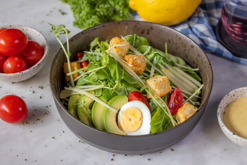 A vibrant salad featuring fresh greens, cherry tomatoes, avocado slices, croutons, and a boiled egg, garnished with herbs and served with dressing.
